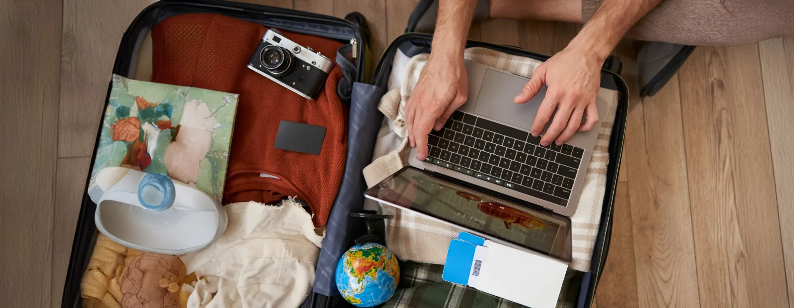 Jeune actif faisant sa valise tout en travaillant sur son ordinateur portable